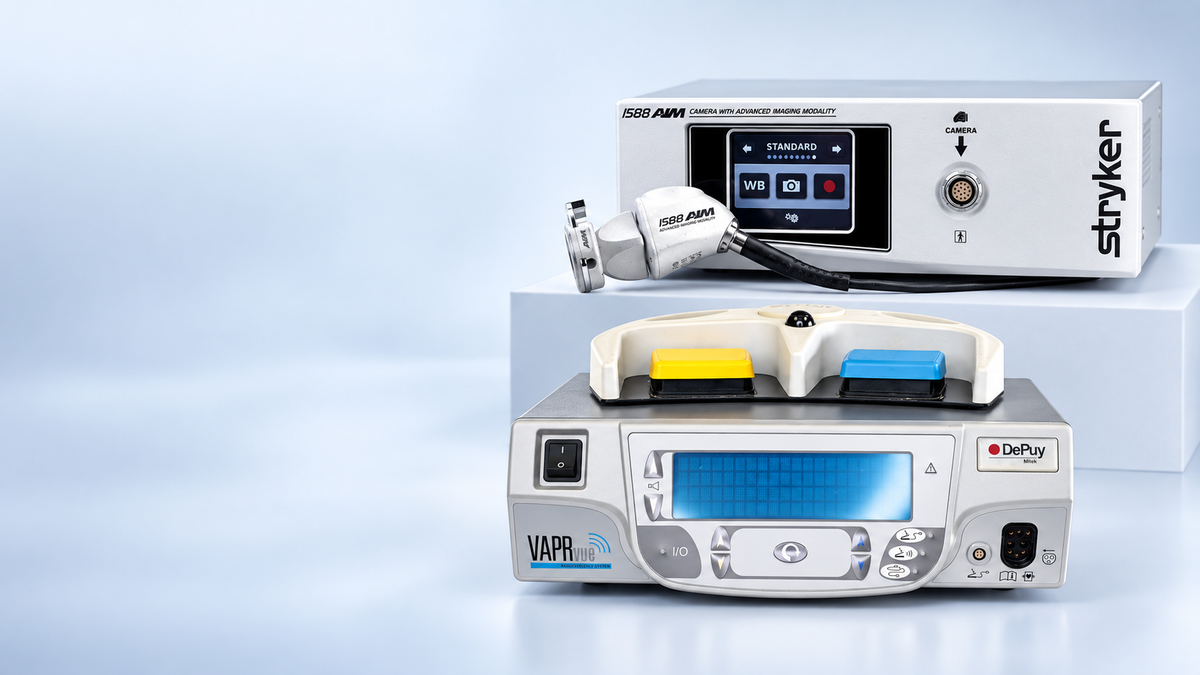 Two medical-grade electronic devices displayed together on a clean light blue studio background. The upper device is white with a black display screen and the brand name Stryker visible on the right side.